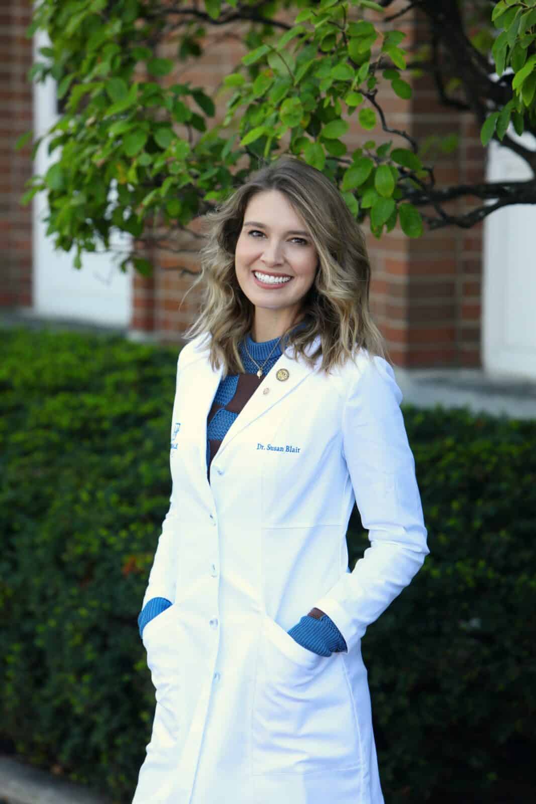 Dr. Susan Blair, Brookfield orthodontist, smiling in a white coat, surrounded by greenery, representing personalized orthodontic care at Hinsdale Orthodontics.